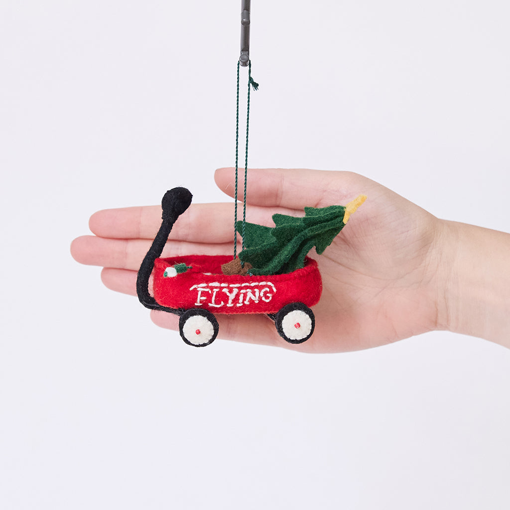 Craftspring’s Little Red Wagon with Tree Ornament displayed in front of a hand to show its size — felt little red wagon carrying a Christmas tree and garland, with embroidered and beaded details, a charming heirloom-quality piece for Christmas gifting — ethically crafted by artisans using sustainable wool.
