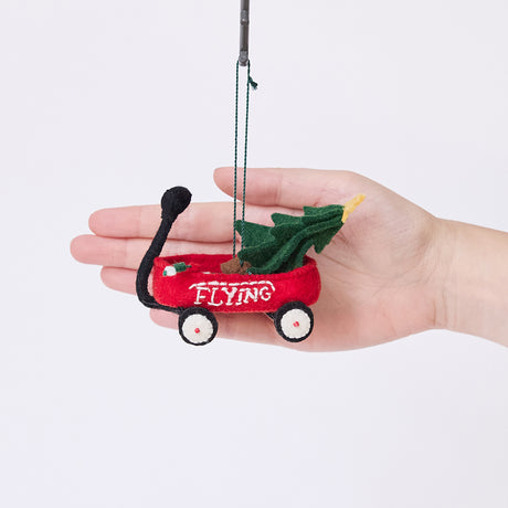 Craftspring’s Little Red Wagon with Tree Ornament displayed in front of a hand to show its size — felt little red wagon carrying a Christmas tree and garland, with embroidered and beaded details, a charming heirloom-quality piece for Christmas gifting — ethically crafted by artisans using sustainable wool.