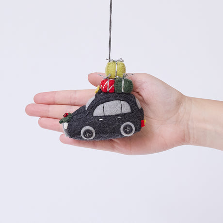 Craftspring’s London Black Cab ornament held in front of a hand to show its size—handmade from sustainable wool with beaded and embroidered details, presents on top of the car, and holly accents, ethically crafted by artisans using sustainable wool.