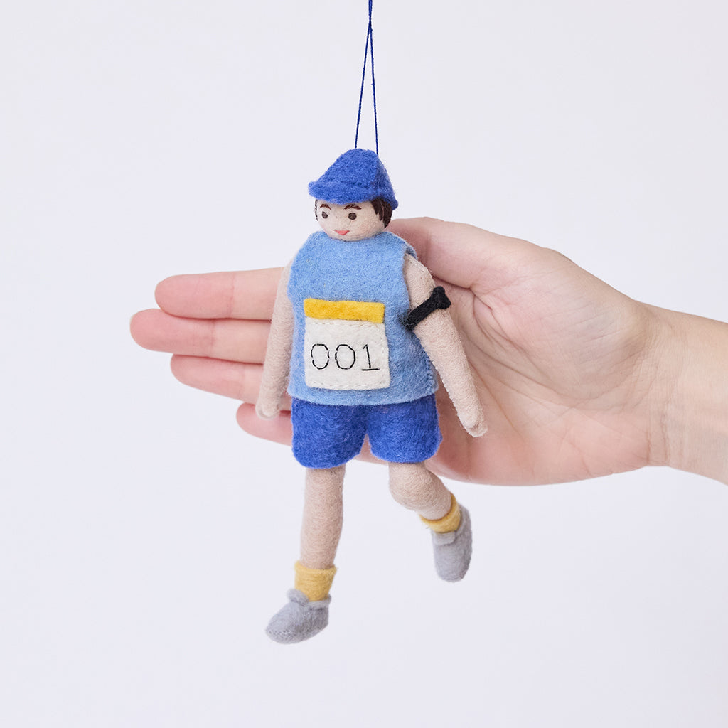 Craftspring’s Marathon Runner ornament held in front of a hand to show its size—handmade from sustainable wool with a race bib numbered 001 and an armband, ethically crafted by artisans using sustainable wool.