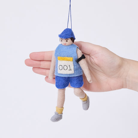 Craftspring’s Marathon Runner ornament held in front of a hand to show its size—handmade from sustainable wool with a race bib numbered 001 and an armband, ethically crafted by artisans using sustainable wool.