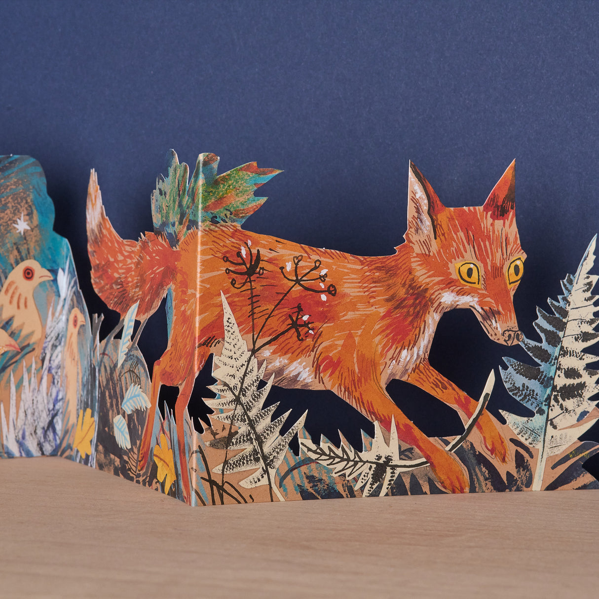 Step into a moonlit woodland scene with this beautifully illustrated tri-fold card by celebrated British artist Mark Hearld. Rich in atmosphere and storytelling, the artwork captures a fox on a quiet nocturnal wander through the forest—watched closely by hens, partridge, and other woodland creatures, while a delicate bunny hides among the grasses.