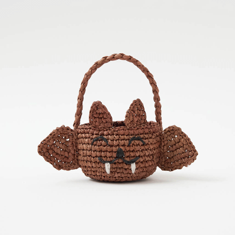 A hand-crocheted raffia Mini Bat Basket featuring playful wings, pointed ears, tiny fangs, and a sweet embroidered face for Halloween treats, treasures, and imaginative play.
