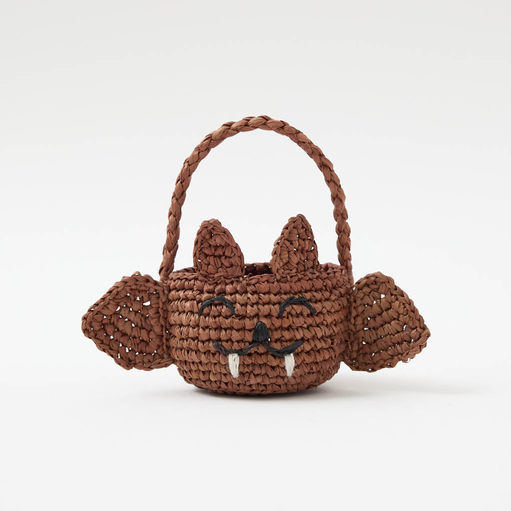 A hand-crocheted raffia Mini Bat Basket featuring playful wings, pointed ears, tiny fangs, and a sweet embroidered face for Halloween treats, treasures, and imaginative play.