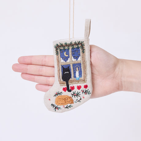 Craftspring’s Holiday Cats Mini Stocking ornament held in front of a hand to show its size—handmade from linen with intricate beaded and embroidered details of a cozy holiday scene with two cats and a window, ethically crafted by artisans using sustainable materials.
