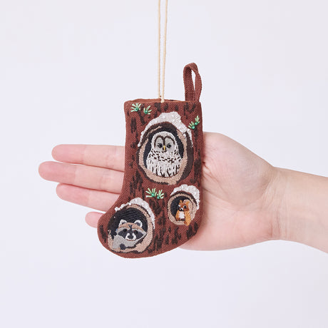 Craftspring’s Woodland Mini Stocking ornament held in front of a hand to show its size—handmade from linen with intricate beaded and embroidered details, including an owl, raccoon, and squirrel peeking out of holes in a tree, ethically crafted by artisans using sustainable materials.