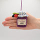 Hand-felted wool ornament of a berry jam jar with a red gingham-patterned lid, topped with beaded blackberry and raspberry accents. Crafted with embroidered details and soft textures, it includes a hanging string and measures approximately 2.75 inches high. A sweet, handmade tribute to homemade preserves and cozy kitchen moments. Held in a hand for scale
