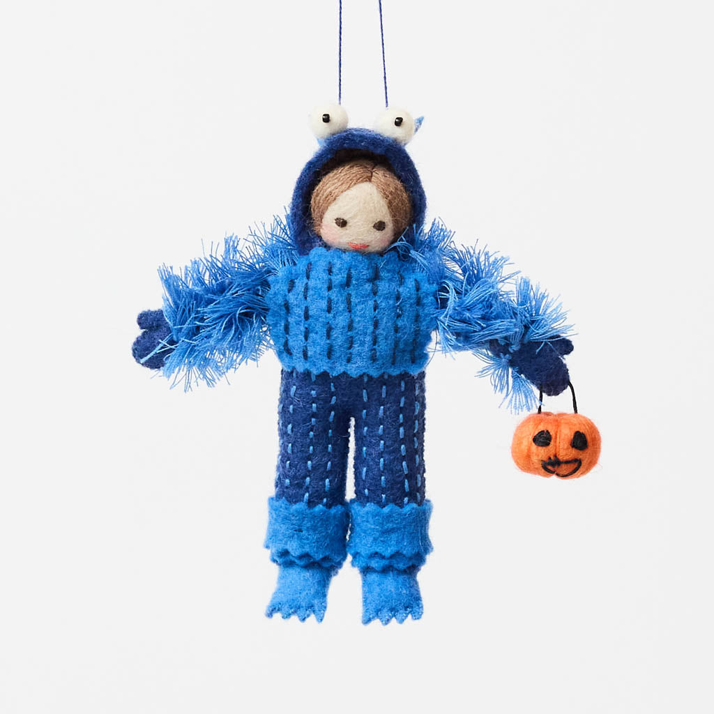 A handmade felt Monster Trick-or-Treater Ornament featuring a child dressed in a fuzzy blue monster costume and carrying a miniature jack-o’-lantern candy bucket.
