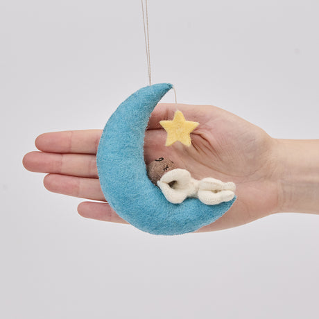 Handmade felt Moon Dreamer Baby Ornament – Brown from Craftspring held in front of a hand to show size—featuring a sleeping baby with brown skin on a crescent moon with a dangling star, adorned with delicate embroidered details, ethically crafted by artisans using sustainable wool.