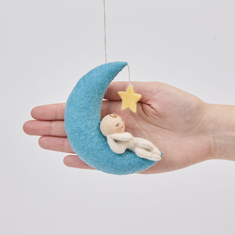 Handmade felt Moon Dreamer Baby Ornament – Light from Craftspring held in front of a hand to show size—featuring a sleeping baby with light skin on a crescent moon with a dangling star, with delicate embroidered details, ethically crafted by artisans using sustainable wool.
