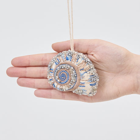 Craftspring’s Moon Snail Shell Ornament displayed in front of a hand to show its size — made of satin with intricate beaded and embroidered details, ethically crafted by artisans.