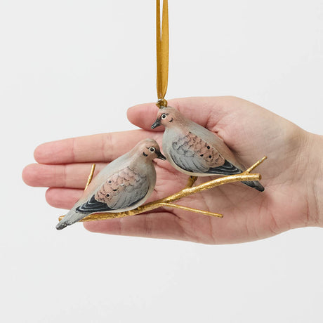 Two little doves, perched side by side. Our Mourning Doves Ornament captures one of nature’s sweetest pairings, with two beautifully hand-painted birds resting together on a delicate gold-toned metal branch.