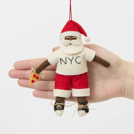 Celebrate Christmas in the Big Apple with our handmade NYC Santa Ornament, featuring a deep brown Santa dressed like a true New Yorker in an NYC tee and sneakers, with a classic slice of New York pizza in hand.