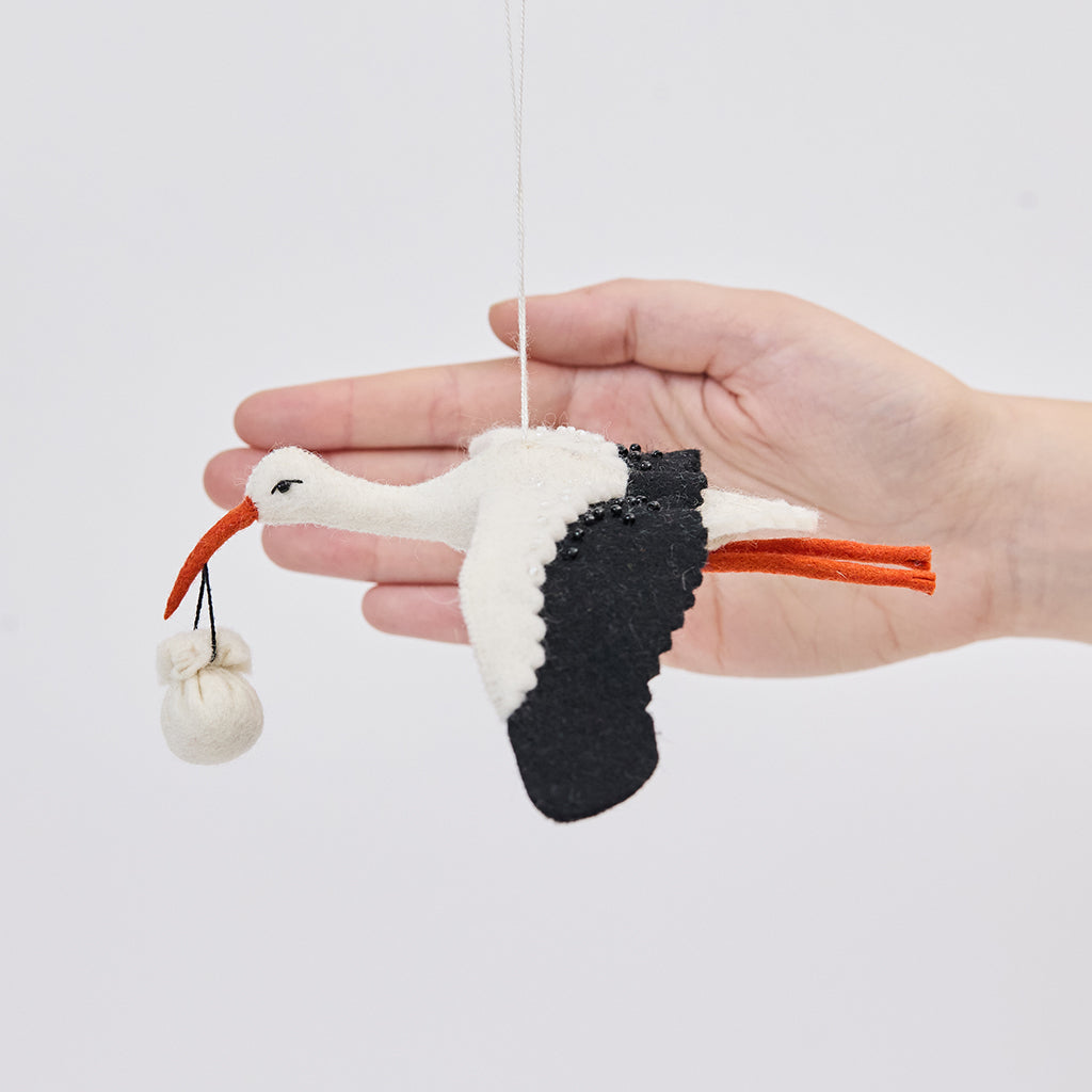 Handmade felt New Baby Stork ornament from Craftspring held in front of a hand to show size—featuring a stork carrying a bundle with intricate beaded and embroidered details, showcasing artisan craftsmanship and heirloom quality, ethically crafted using sustainable wool.