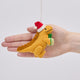 Handmade felt Orange T-Rex Dinoclaus ornament from Craftspring held in front of a hand to show its size—featuring an orange dinosaur wearing a red Santa hat and holding a green present, perfect for dino-loving kids and playful holiday gifting, ethically crafted by artisans using sustainable wool.
