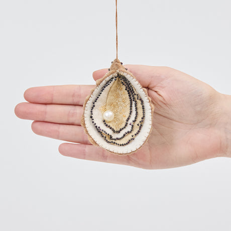 Craftspring’s handmade felt Oyster ornament held in front of a hand to show its size—features a beaded pearl and intricate beaded and embroidered details, ethically crafted by artisans using sustainable wool.