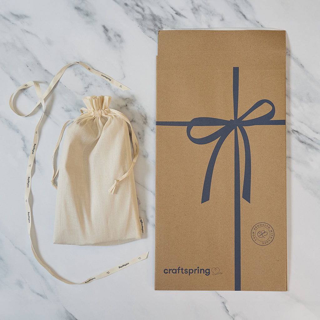 Craftspring packaging for Vintage-Style Angel Bundle of three angel ornaments, featuring a branded mailer and protective cloth bag displayed on a marble surface — ready to safely deliver handmade felt holiday decor with beaded and embroidered details, ethically crafted by artisans using sustainable wool.