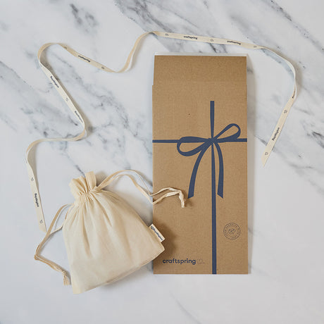 Craftspring packaging for Goose Ornament, featuring a branded mailer and protective cloth bag displayed on a marble surface — ready to safely deliver heirloom-quality, ethically crafted felt decor from artisans using sustainable wool.