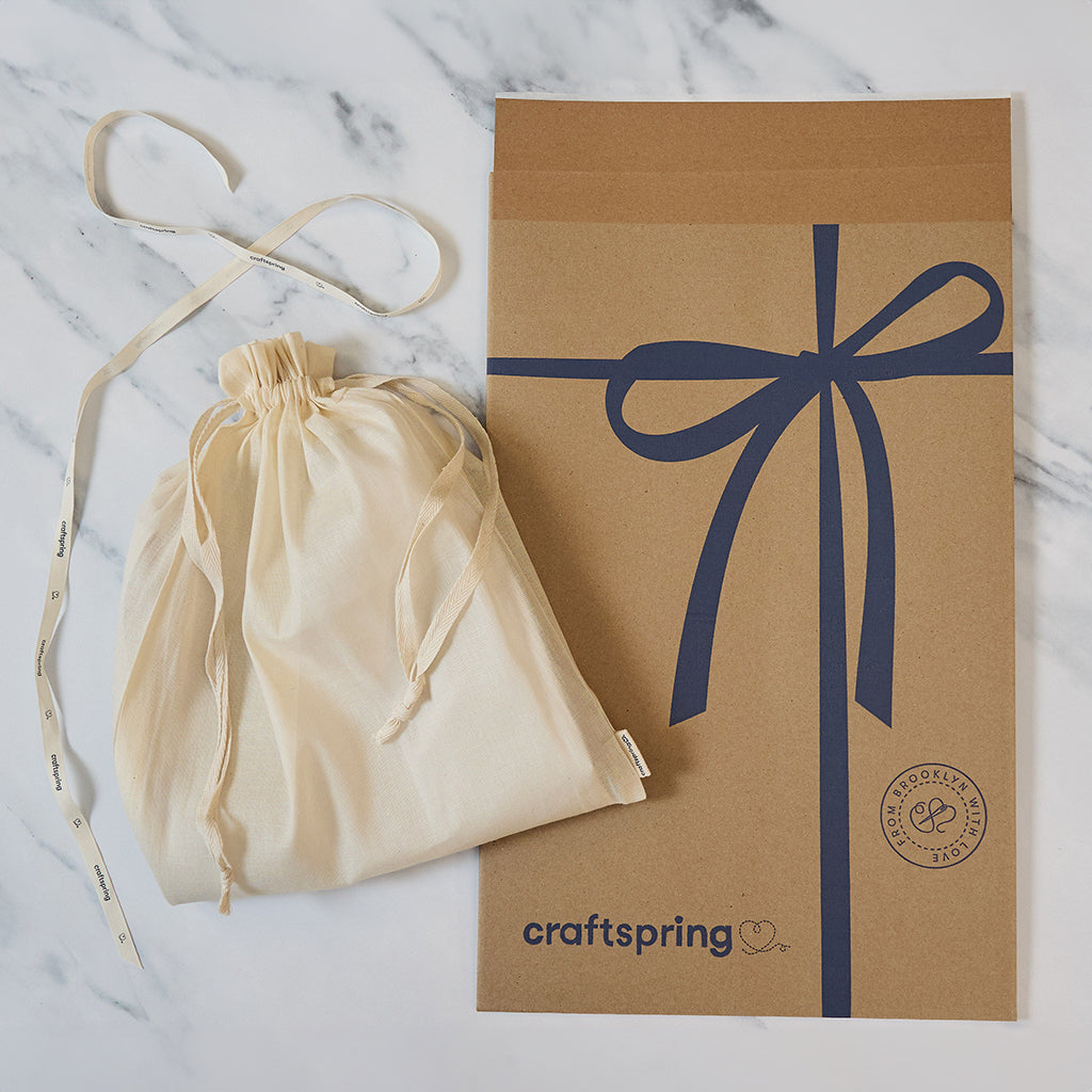 Craftspring packaging for the Nativity Barn, featuring a branded mailer and protective cloth bag displayed on a marble surface — ready to safely deliver handmade felt holiday decor, ethically crafted by artisans using sustainable wool.