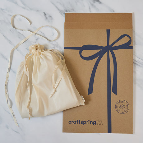 Craftspring packaging for the Nativity Barn, featuring a branded mailer and protective cloth bag displayed on a marble surface — ready to safely deliver handmade felt holiday decor, ethically crafted by artisans using sustainable wool.