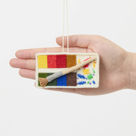 A small celebration of color in miniature form, our Paint Palette Ornament captures the familiar beauty of an artist’s workspace. Soft blocks of felted color sit alongside a tiny paintbrush with splashing embroidered brushstrokes, as if paused mid-creation.