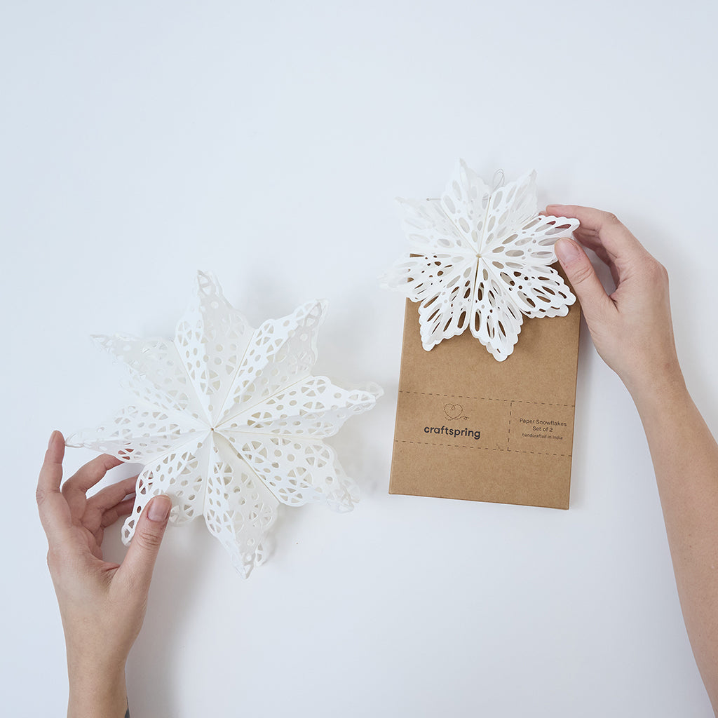 Craftspring’s Paper Snowflakes Christmas Ornaments — Set of 2, large white snowflakes with intricate cutout patterns, one slightly larger than the other —  ethically handmade by artisans from recycled cotton waste.