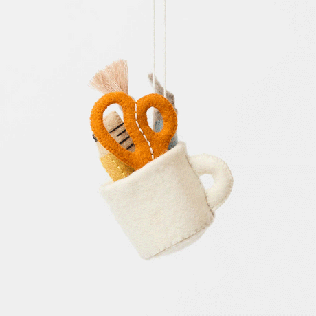 Bring the charm of the classroom and the drafting table to your holiday décor with our&nbsp;Pencil Cup Felt Ornament. This handcrafted design features a soft wool felt mug filled with iconic school and creative essentials—bright scissors, a pencil, a paintbrush, a fountain pen, and a ruler—capturing the everyday magic of learning and creativity.&nbsp;
