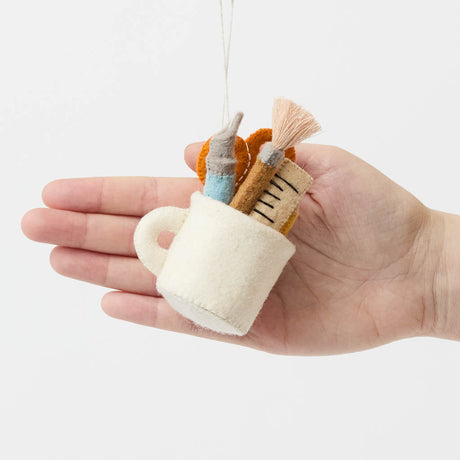 Bring the charm of the classroom and the drafting table to your holiday décor with our&nbsp;Pencil Cup Felt Ornament. This handcrafted design features a soft wool felt mug filled with iconic school and creative essentials—bright scissors, a pencil, a paintbrush, a fountain pen, and a ruler—capturing the everyday magic of learning and creativity.&nbsp;