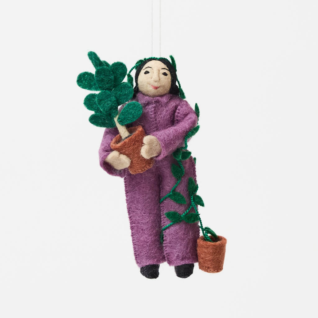 For the person who always has room for just one more plant, our Plant Parent Ornament celebrates the love, care, and wonderfully leafy obsession of keeping a home full of green things. Handcrafted from natural wool by skilled artisans, this whimsical felt ornament features a proud plant parent dressed in purple and happily surrounded by an abundance of potted greenery.