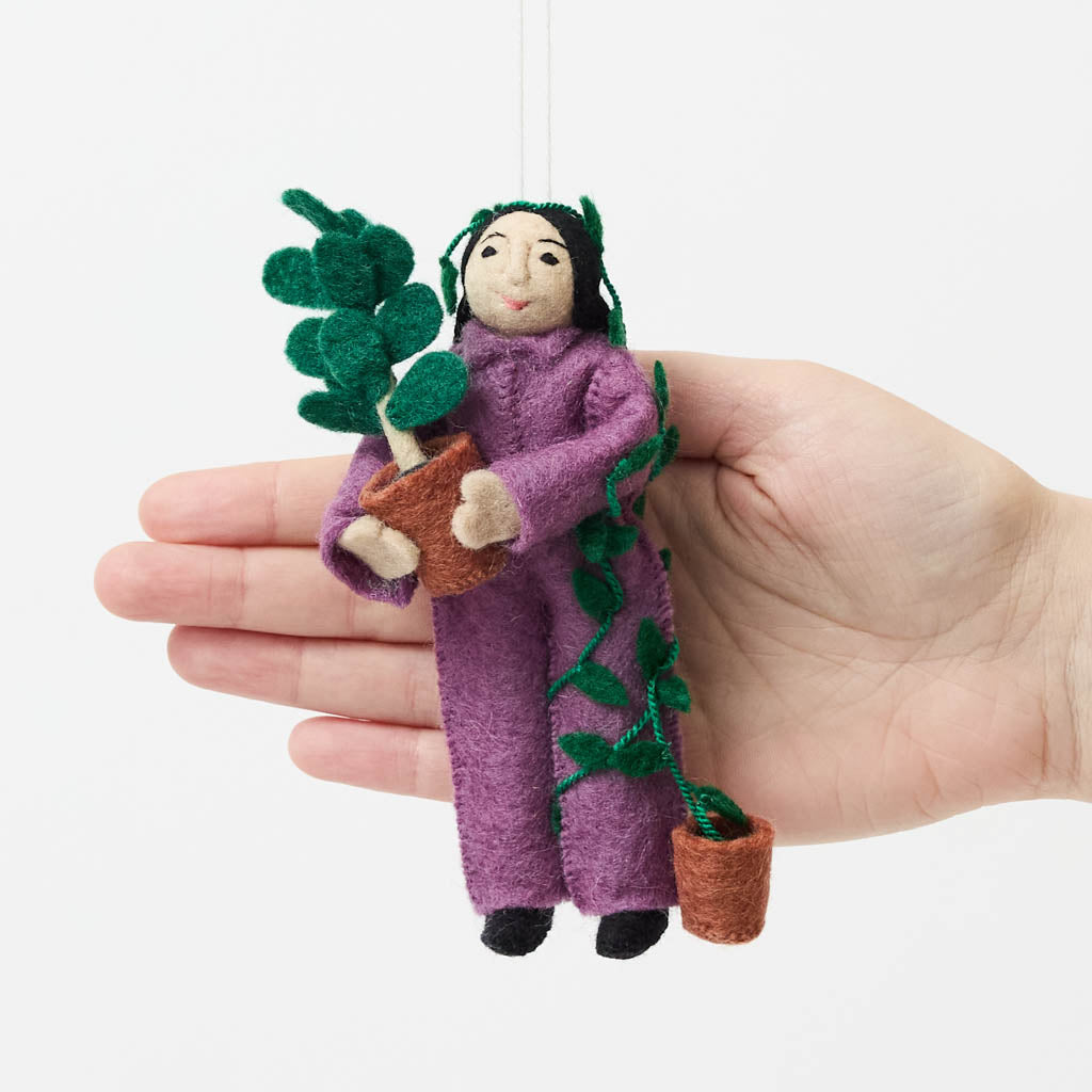 For the person who always has room for just one more plant, our Plant Parent Ornament celebrates the love, care, and wonderfully leafy obsession of keeping a home full of green things. Handcrafted from natural wool by skilled artisans, this whimsical felt ornament features a proud plant parent dressed in purple and happily surrounded by an abundance of potted greenery.