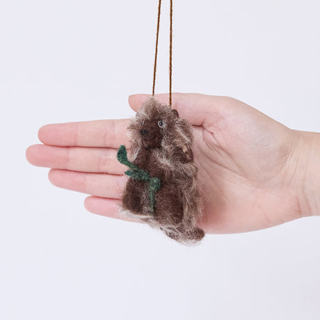 Craftspring’s Porcupine ornament held in front of a hand to show its size — handmade from sustainable wool with fuzzy quills, a leafy branch, and a charming face, ethically crafted by artisans.