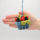Hand-felted ornament of a wool pint container filled with beaded raspberries and blackberries, sparkling with embroidered detail. Designed to resemble a farmer’s market berry basket, this 2.25-inch tall ornament includes a hanging string. A colorful and cozy holiday gift for foodies, gardeners, or fans of cottagecore and handmade treasures. With hand for scale.