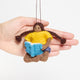 Handmade felt ornament of a young girl sitting cross-legged, absorbed in a book. Crafted from natural merino-blended wool, her focused gaze and relaxed posture capture the magic of reading. With braided brown hair and a warm-toned complexion, this ornament adds a cozy, literary touch to reading nooks, desks, or shelves. A perfect gift for bookworms, young readers, or anyone who treasures the quiet joy of a good story. Ready to hang with a string attached.