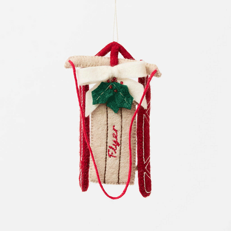 Our Red Flyer Sled Ornament captures the nostalgia of childhood winters and treasured holiday traditions. Inspired by classic wooden sleds, this charming keepsake features bright red runners, a cozy neutral-toned seat embroidered with "Flyer," and a festive holly sprig nestled beneath a soft white bow.