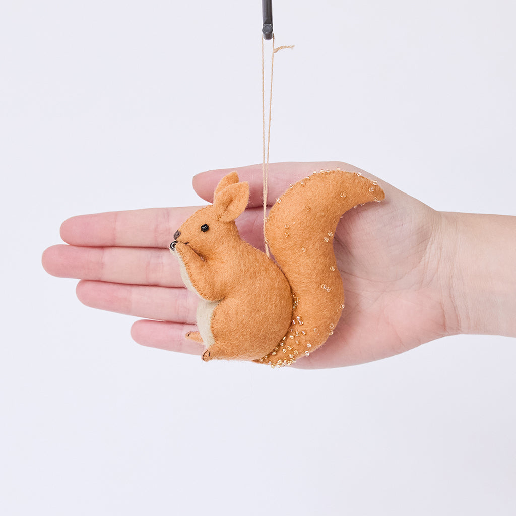Craftspring’s Red Squirrel ornament held in front of a hand to show its size—handmade from sustainable wool with delicate beaded and embroidered details, ethically crafted by artisans using sustainable wool.