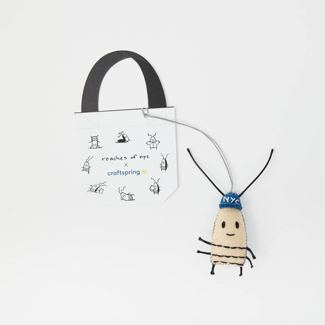 Handcrafted from natural wool felt, our surprisingly adorable cockroach bag charm features a sweet embroidered smile, playful antennae, tiny legs, and a bright blue beanie embroidered with “NYC.” Full of personality and unmistakable New York attitude, this quirky little companion brings a touch of city mischief to your everyday style.