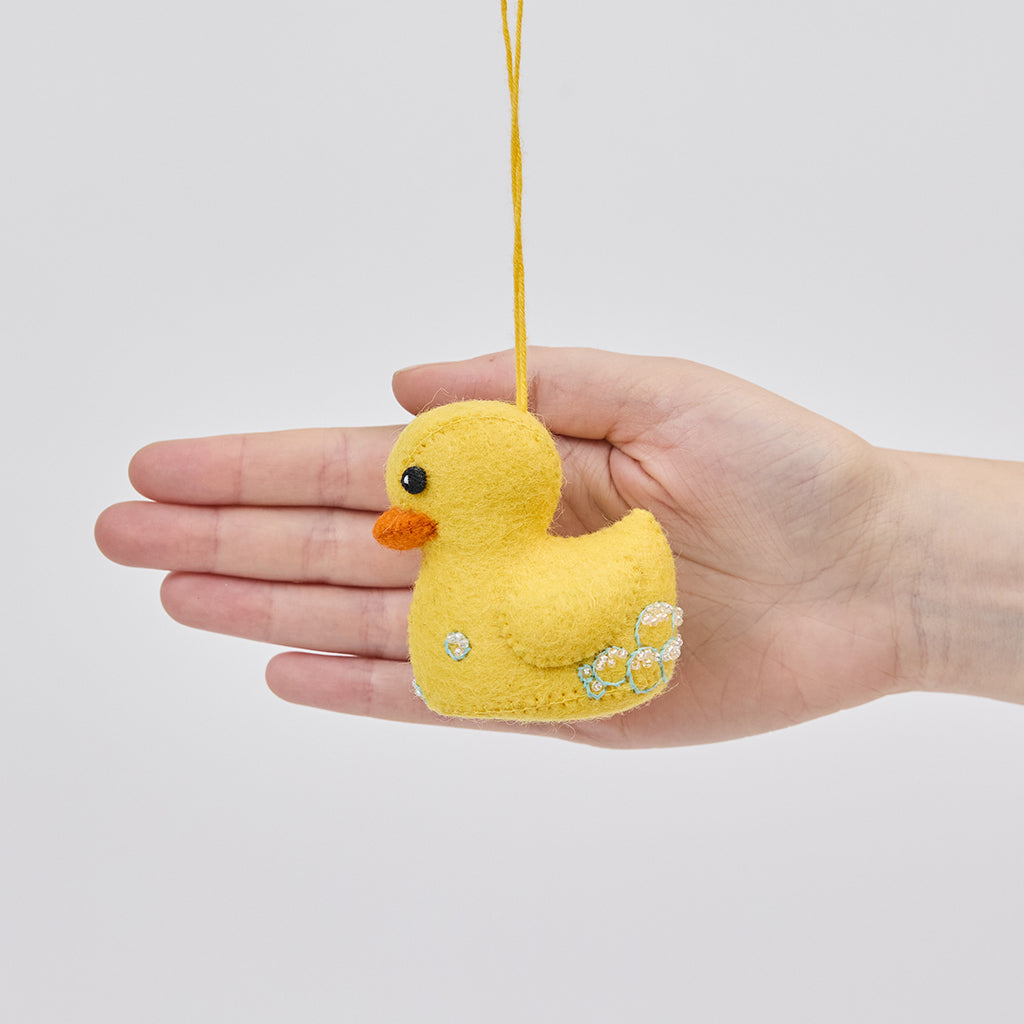 Handmade felt Rubber Duck ornament from Craftspring held in front of a hand to show size—featuring detailed embroidered and beaded soap bubbles, showcasing artisan craftsmanship and playful charm, ethically crafted by artisans using sustainable wool.