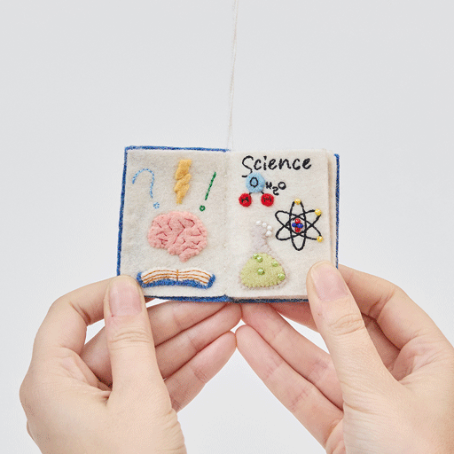 Handmade felt STEAM Book ornament from Craftspring shown flipping through interior pages—featuring intricate beaded and embroidered details for Science, Technology, Engineering, Arts, and Math, ethically crafted by artisans using sustainable wool.