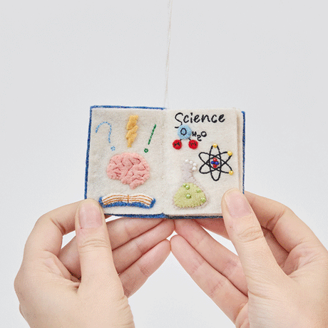 Handmade felt STEAM Book ornament from Craftspring shown flipping through interior pages—featuring intricate beaded and embroidered details for Science, Technology, Engineering, Arts, and Math, ethically crafted by artisans using sustainable wool.