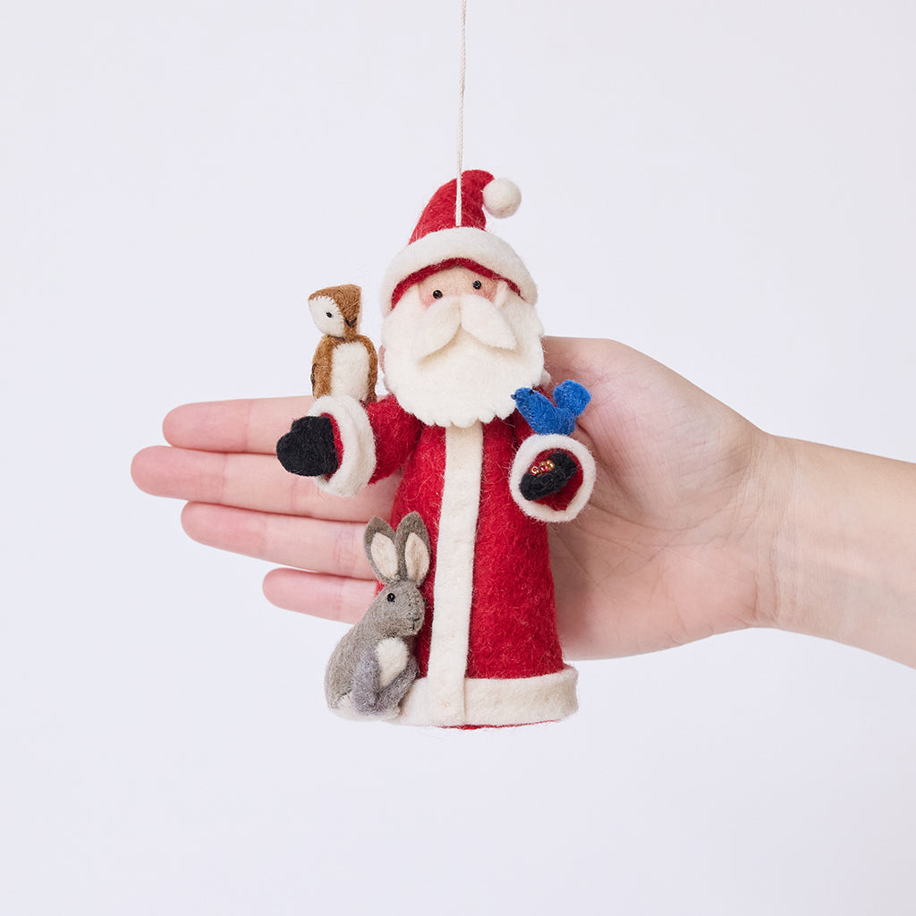Craftspring’s Santa with Woodland Animals ornament held in front of a hand to show its size—handmade from sustainable wool with a Santa holding beaded birdseed, a bunny next to him, and an owl and bluebird perched on his arms, ethically crafted by artisans using sustainable wool.