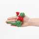 Handmade felt Santasaurus T-Rex ornament from Craftspring held in front of a hand to show size—featuring a red Santa hat, red sweater, and embroidered details, perfect for dino-loving kids and festive holiday gifting, ethically crafted using sustainable wool.