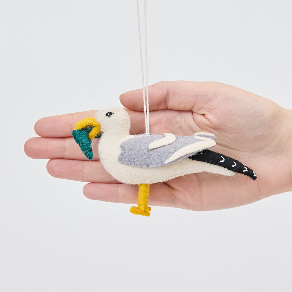 Handmade felt Seagull ornament from Craftspring held in front of a hand to show its size—featuring embroidered details and a fish in its beak, sustainably handmade by artisans using wool.