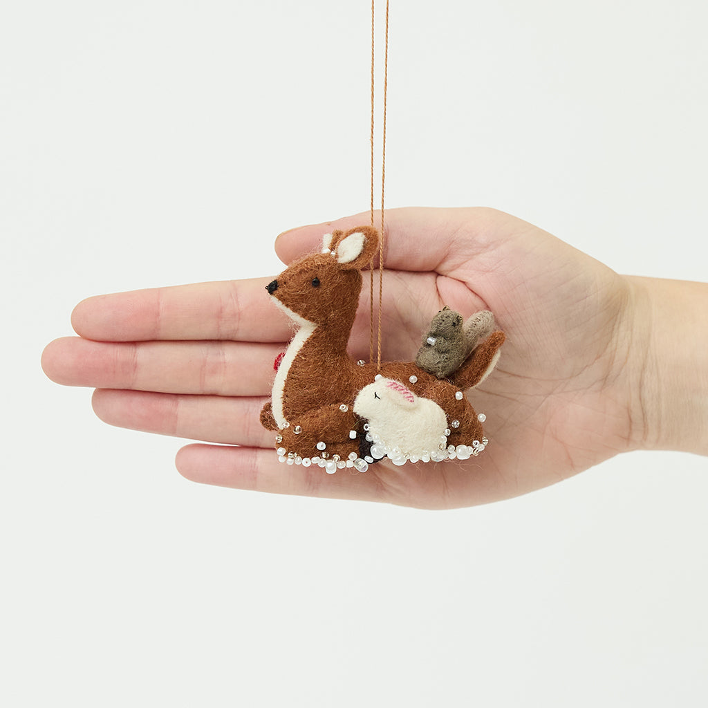 Craftspring’s Sitting Deer with Friends Ornament in front of a hand to show its size—handmade from sustainable wool, featuring a deer with a rabbit, squirrel, and bird, with delicate beaded and embroidered details, ethically crafted by artisans using sustainable wool.