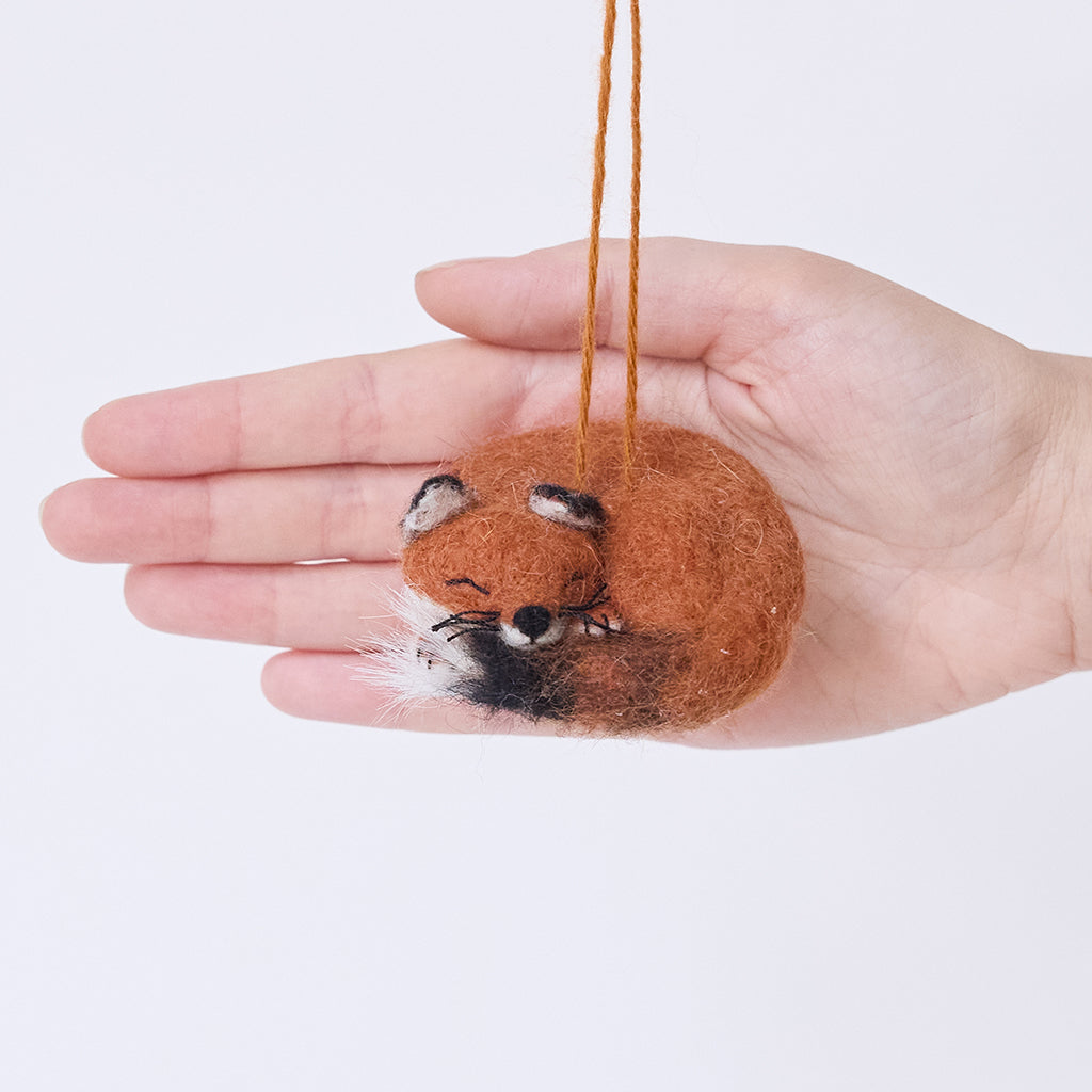 Craftspring’s Sleepy Fox Ornament displayed in front of a hand to show its size — curled up with a cute face, fluffy tail, and whiskers, a sweet heirloom-quality piece perfect for Christmas gifting — ethically crafted by artisans using sustainable wool.