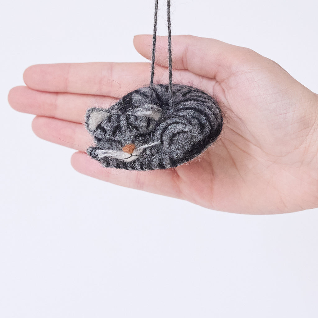 Craftspring’s Sleepy Gray Cat Ornament displayed in front of a hand to show its size—needle-felted with whiskers and a charming face, ethically crafted by artisans using sustainable wool.