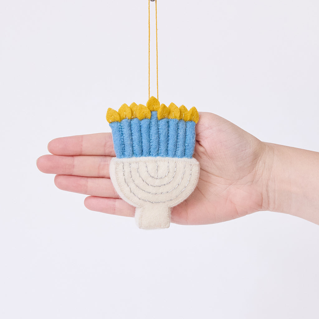 Craftspring’s Small Silver Menorah ornament displayed in front of a hand to show its size — handmade from sustainable wool with silver embroidery and blue candles, ethically crafted by artisans for meaningful Hanukkah and holiday gifting.