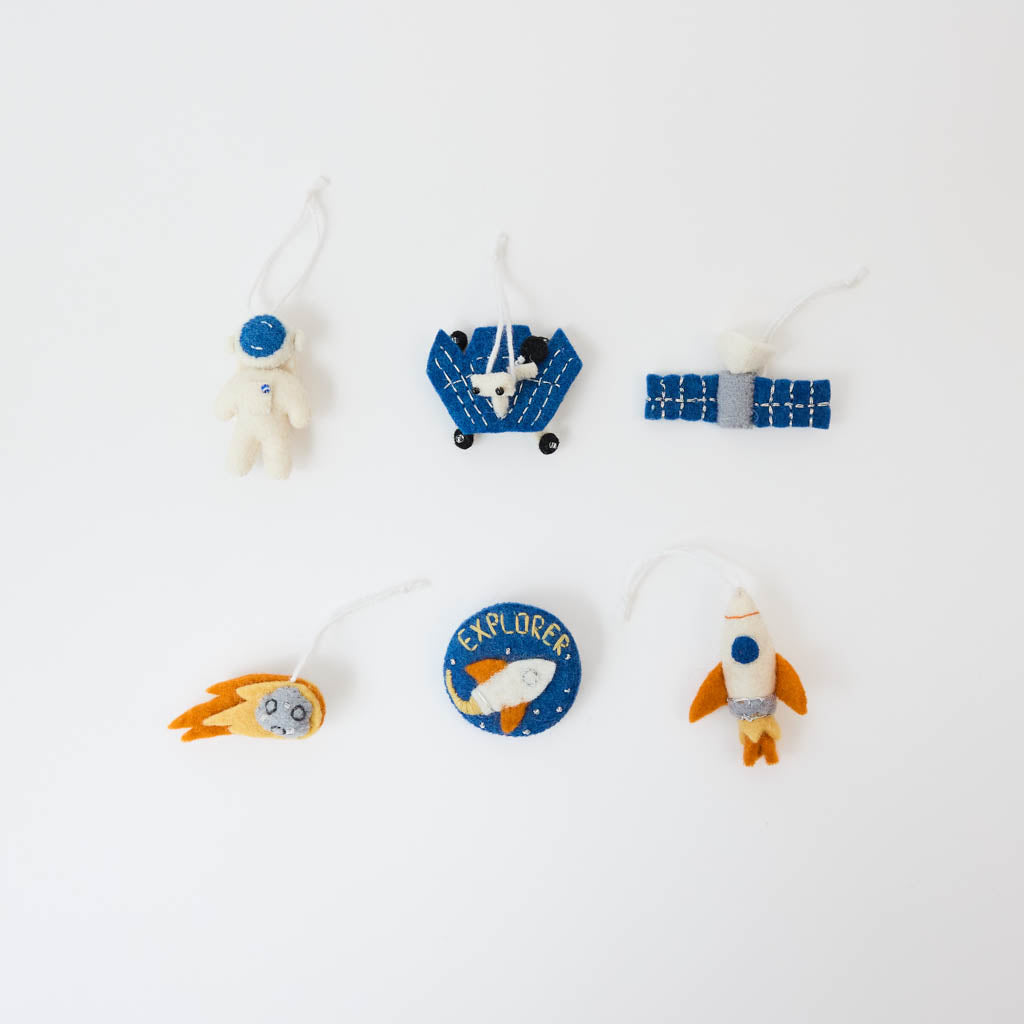 Blast off into a universe of discovery with our Space Mini Ornaments Set. This delightful collection includes five handcrafted felt ornaments inspired by the wonders of space: an astronaut, satellite, space shuttle, rocket ship, and meteor, along with a coordinating Explorer badge that can be displayed as a keepsake or worn as a symbol of curiosity and adventure.