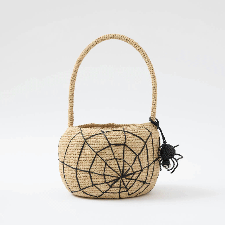 A hand-crocheted raffia Spider Basket featuring a bold black spiderweb and playful spider detail, perfectly sized for trick-or-treating, Halloween treasures, and festive fall displays.