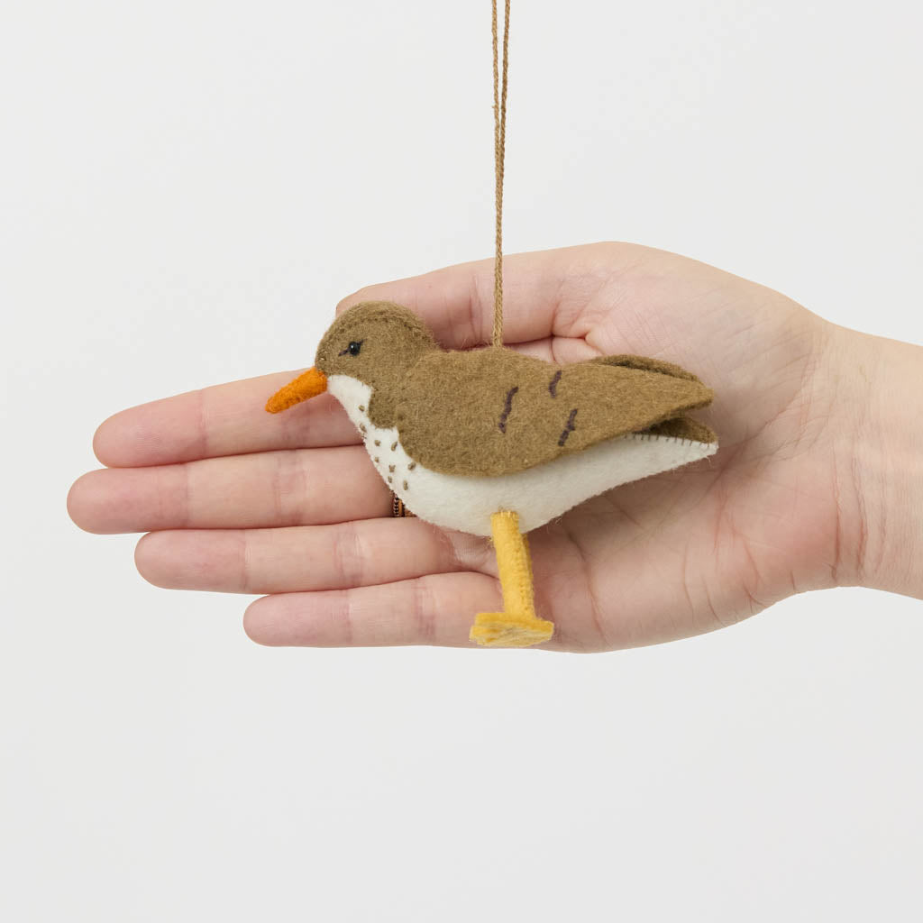 Bring a touch of the shoreline to your holiday décor with our delightful Spotted Sandpiper Ornament. Carefully handcrafted from eco-friendly wool felt, this charming bird captures the distinctive features of the beloved sandpiper, from its warm brown plumage and bright orange beak to its delicate spotted breast.