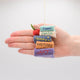 Handmade felt ornament featuring a miniature stack of colorful books, meticulously crafted from natural wool using traditional felting techniques. This eco-friendly and lightweight ornament adds a cozy, literary touch to holiday trees, bookshelves, or reading nooks. A charming gift for bookworms, teachers, and students, perfect for any occasion or year-round decor. Hand in photo for scale reference.